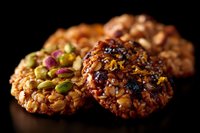 Homemade granola cookies with mixed nuts, seeds, and dried fruits on dark background. Close-up macro shot shows rich texture and natural ingredients.