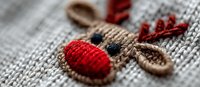 Handcrafted reindeer embroidery on gray knitted fabric, festive Christmas textile decoration with red nose and antlers detail.