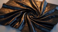 Luxurious metallic fabric with golden bronze and deep blue hues twisted in elegant flowing folds, showcasing rich textile texture and dramatic light reflections.