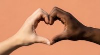 Two diverse hands forming heart shape symbol representing unity love and racial harmony on coral background for social campaigns and diversity projects.