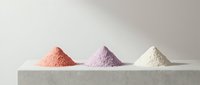 Three colorful powder piles in pink, purple and white arranged on clean white surface for cosmetic and beauty product applications.