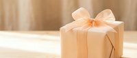 Elegant gift box wrapped in kraft paper with a soft peach ribbon bow on a wooden surface, warm neutral tones for holiday or celebration concepts.