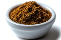 Ground cinnamon powder in white ceramic bowl on white background, macro shot with selective focus showing aromatic spice texture and detail.
