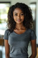 Young African American woman with curly hair wearing gray t-shirt smiling at camera in modern indoor setting for lifestyle and portrait photography.