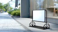 Empty white board stand with decorative metal frame on stone pavement near glass storefront entrance, outdoor advertising mockup for restaurant or retail.