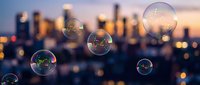 Soap bubbles floating against blurred city skyline at sunset with warm golden light and bokeh effects creating dreamy urban atmosphere.