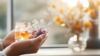Gentle hands holding glass jar with glowing candle and delicate dried flowers against soft window light, creating cozy atmospheric mood for wellness and mindfulness.