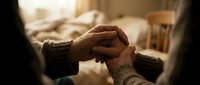 Elderly couple holding hands in warm sunlight showing love, care and support in cozy bedroom setting with soft lighting creating intimate romantic atmosphere.