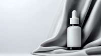 White cosmetic dropper bottle on elegant gray silk fabric background with soft folds and shadows, mockup for skincare product presentation.