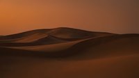 Desert sand dunes landscape with warm orange sunset glow creating dramatic shadows and curves in arid wilderness environment for travel and nature themes.