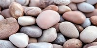 Smooth river stones in natural earth tones create calming texture for spa wellness meditation zen garden landscaping home decor background design projects.