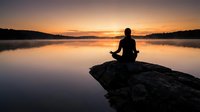 Silhouetted person meditating on rock overlooking calm lake at sunset, peaceful mindfulness and wellness scene for relaxation and mental health content.