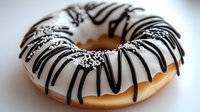 Glazed donut with white frosting and dark chocolate drizzle topped with sprinkles on light background, close-up view of sweet pastry dessert.