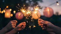 Hands holding lit sparklers at dusk with bokeh lights in background, celebrating festive occasions, holidays, new year events, parties, and outdoor gatherings.