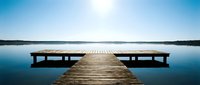 Wooden dock extending into calm blue lake with benches on either side, serene water landscape for relaxation and meditation concepts.
