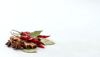 Aromatic spices including star anise, cinnamon sticks, dried chili peppers and bay leaves arranged on white background for culinary and cooking projects.