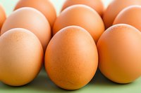 Fresh brown chicken eggs arranged in rows on green surface, showing natural texture and warm tones in macro photography for food industry and packaging design.