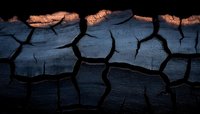 Dramatic close-up of charred wood texture with glowing orange embers and deep cracks forming abstract pattern against dark background. Natural destruction concept.