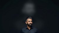 Middle-aged man with dark beard and hair wearing black shirt against dark background. Studio portrait for business, corporate, or professional headshot use.