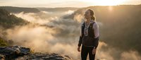 Middle-aged Caucasian male hiker with backpack standing on rocky cliff overlooking misty valley at golden hour sunrise, adventure travel concept.