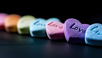 Colorful candy hearts with love messages arranged in line on dark background, selective focus on purple heart. Romantic holiday concept for valentines design.