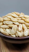 Fresh peeled blanched almonds in brown ceramic bowl on wooden surface, macro food photography showing texture and natural color of nuts.