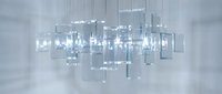 Modern glass cube chandelier with LED lights suspended in minimalist white interior space creating elegant contemporary lighting design for luxury homes.