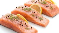 Fresh salmon fillets with lemon slices, dill herbs and black peppercorns on white background. Raw fish portions ready for cooking and healthy meal preparation.