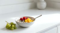 Ceramic bowl filled with mixed fresh berries and diced mango, served with spoon on white kitchen counter, healthy breakfast or dessert option.