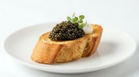 Toasted bread slice topped with creamy spread, luxurious caviar, and fresh herbs on white plate for fine dining and gourmet food concepts.