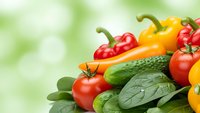 Fresh organic vegetables including colorful bell peppers, tomatoes, cucumber and leafy greens arranged on green bokeh background for healthy eating concepts.