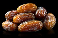 Fresh medjool dates arranged on black background with dramatic lighting showing natural texture and glossy surface, isolated macro food photography.