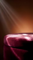Luxurious burgundy velvet podium with golden light rays streaming from above creating dramatic atmosphere for premium product display and presentation.