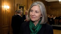Professional mature Caucasian businesswoman with gray hair and green scarf in elegant wood-paneled meeting room during corporate event or conference.