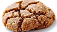 Freshly baked molasses ginger cookie with crackled surface and sugar coating, showing soft chewy texture and deep brown color on white background.