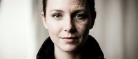 Young Caucasian woman with half face showing severe bruising and injuries from domestic violence or abuse, serious expression against neutral background.