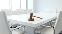Wooden gavel on white conference table in modern meeting room with chairs, representing legal proceedings, justice system, and corporate governance.