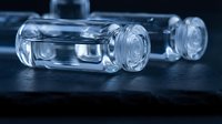 Clear glass medical vials on dark surface for pharmaceutical research and laboratory testing applications in healthcare industry.