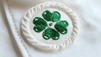 Green four-leaf clover embroidered on white circular fabric patch with decorative stitched border, symbol of luck and Irish heritage, isolated on white background.