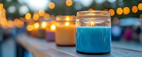 Glowing glass jar with vibrant blue liquid against blurred warm bokeh lights background creates magical ambiance on wooden surface at dusk.