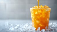 Refreshing iced tea pouring into clear plastic cup with ice cubes on gray background, dynamic splash and golden liquid catching light, summer drink photography.