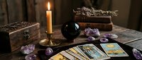 Mystical tarot card reading setup with burning candle, crystal ball, amethyst stones and ancient wooden boxes on dark table for fortune telling sessions.