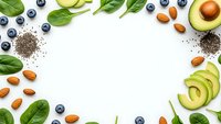 Healthy superfood ingredients frame with avocado, blueberries, spinach, chia seeds and almonds on white background for nutrition and wellness content.
