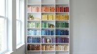 Modern home library with colorful books arranged by rainbow spectrum on white built-in shelves creating organized reading space for interior design.