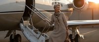Professional African American businesswoman in elegant coat descending private jet stairs at sunset, luxury travel and corporate success concept.