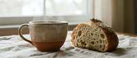 Steaming ceramic mug and sliced artisan sourdough bread on linen cloth by a window, cozy morning breakfast scene with rustic charm.