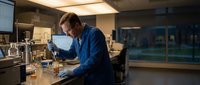 Male scientist in blue lab coat conducting research with microscope in modern laboratory setting for scientific studies and medical analysis.