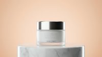 Luxury skincare jar with silver lid displayed on marble platform against warm beige background, suitable for cosmetics and beauty product marketing.