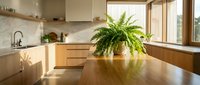 Modern kitchen with wooden cabinetry, marble backsplash, and natural light streaming through large windows, featuring a potted fern plant on the dining table for home decor and interior design inspiration.