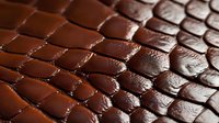 Macro shot of brown leather texture with embossed crocodile or snake skin pattern showing detailed scales, stitching and surface grain. Luxury fashion background.
